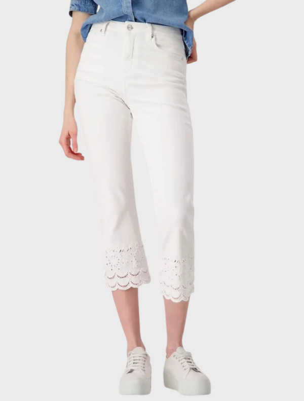 A woman in white jeans and a blue shirt stands confidently, showcasing her stylish outfit.