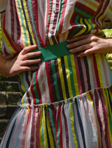 A woman in a striped dress walks leisurely on a path through a natural setting.