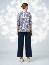 A woman in a floral blouse and wide-leg pants smiles, displaying her chic and vibrant outfit choice.
