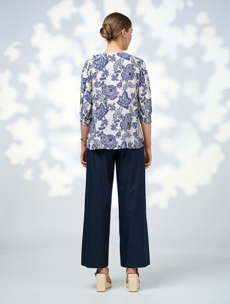 A woman in a floral blouse and wide-leg pants smiles, displaying her chic and vibrant outfit choice.