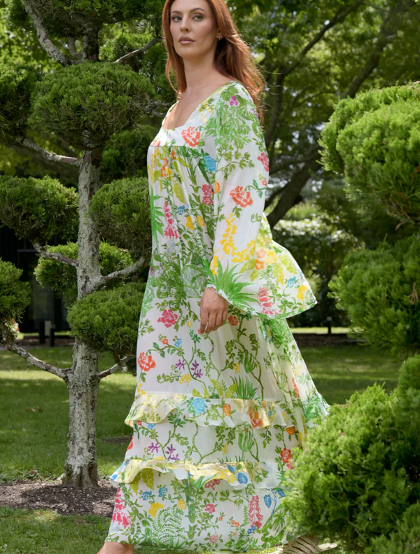 A woman in a floral dress strolls through a park, surrounded by greenery and blooming flowers.