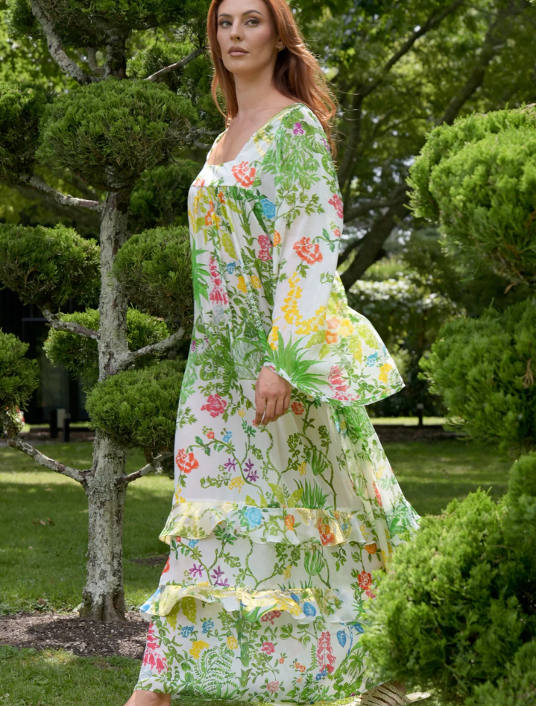 A woman in a floral dress strolls through a park, surrounded by greenery and blooming flowers.