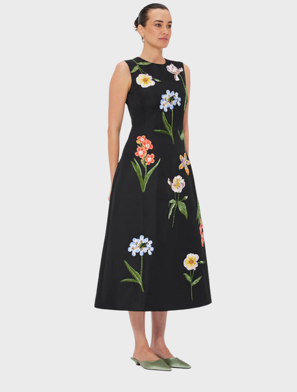 A woman wearing a black dress adorned with floral patterns.