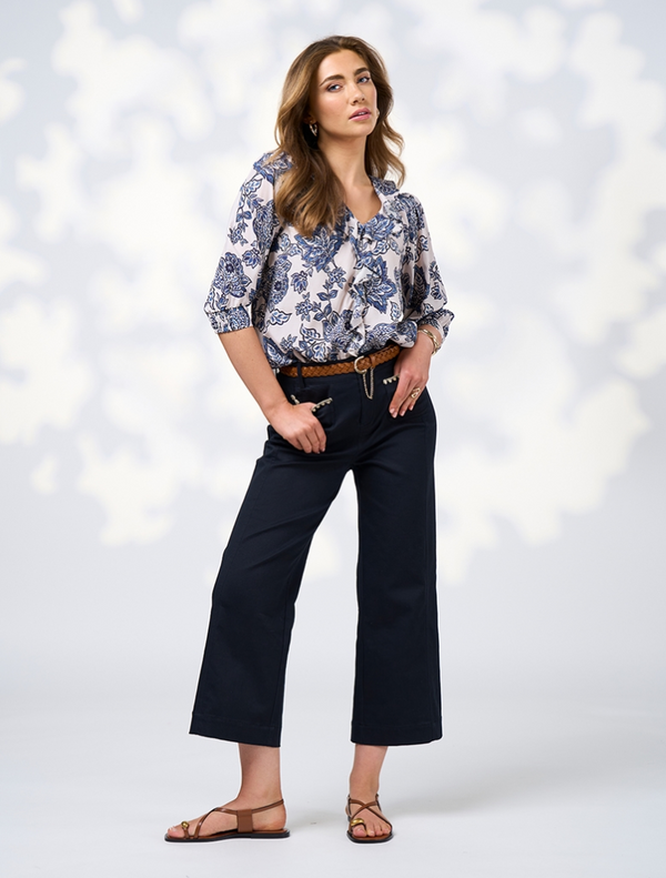 A woman wearing a floral blouse and wide-leg pants stands confidently, showcasing her stylish outfit.