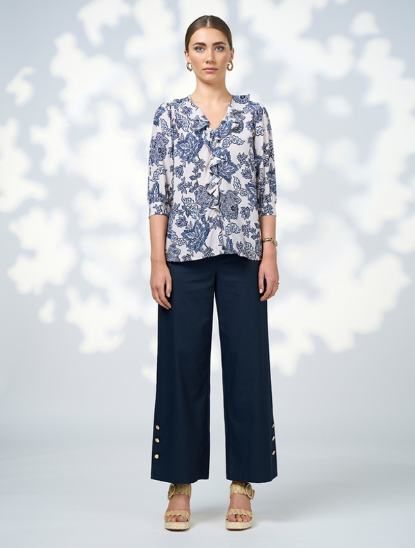 A woman dressed in a floral blouse and wide-leg pants poses, highlighting her fashionable ensemble.