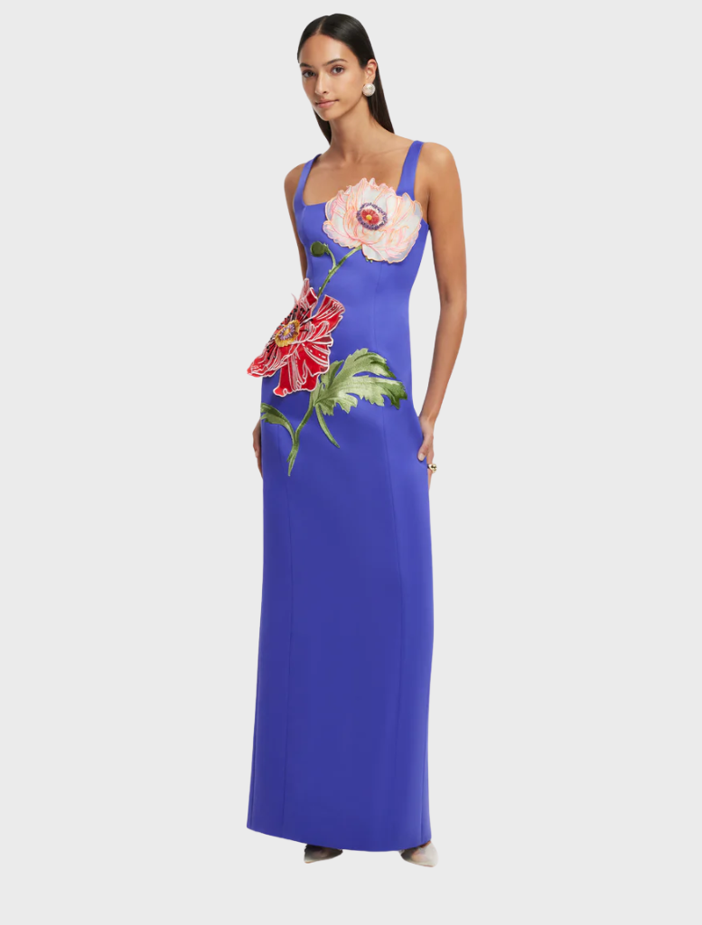 A woman wearing a blue dress stands elegantly, showcasing a stylish design.