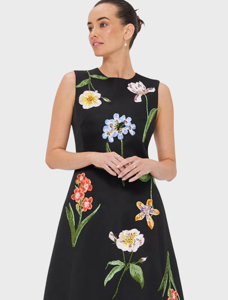 A woman wearing a black dress adorned with floral patterns.