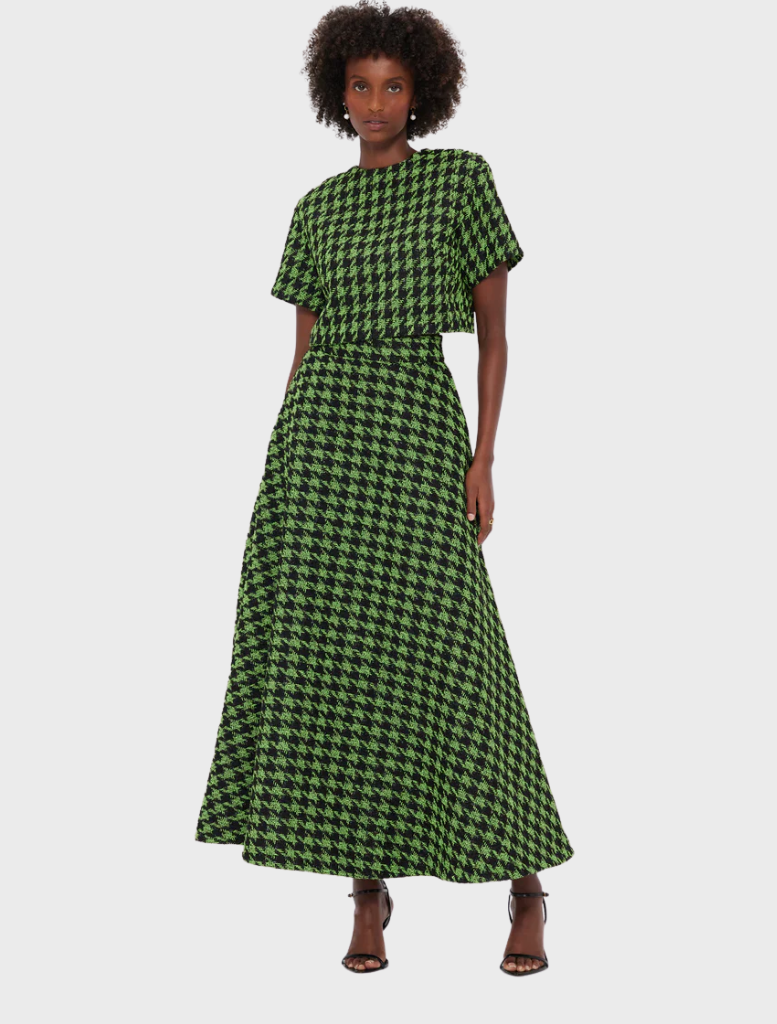 A model poses in a stylish green and black houndstooth dress, featuring a short-sleeve top and a full-length, flowing skirt.