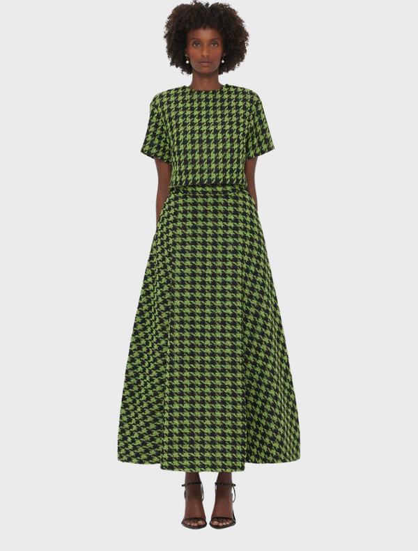 A woman stands facing forward, wearing a green and black houndstooth-patterned Rosalyn-Tweed-Maxi-Skirt with a matching short-sleeve top and black heels.