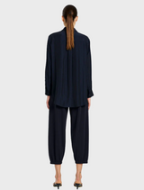 A model dressed in a navy shirt and matching pants stands confidently, showcasing a stylish and coordinated outfit.
