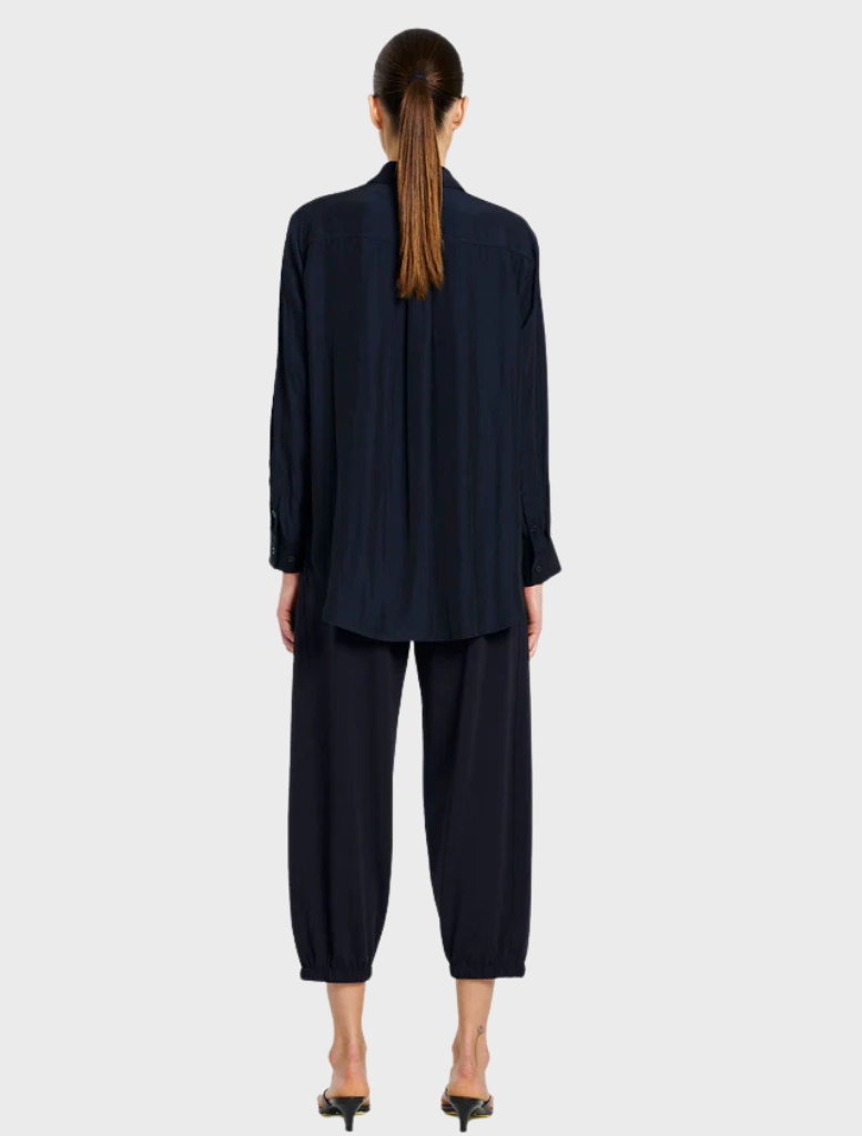 A model dressed in a navy shirt and matching pants stands confidently, showcasing a stylish and coordinated outfit.
