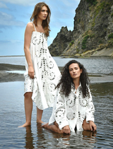 A women in a white dress stands on the sandy beach, with the sea breeze gently tousling her hair.