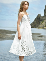 A woman in a white dress stands on the beach, her hair blowing in the wind as she looks out at the sea.