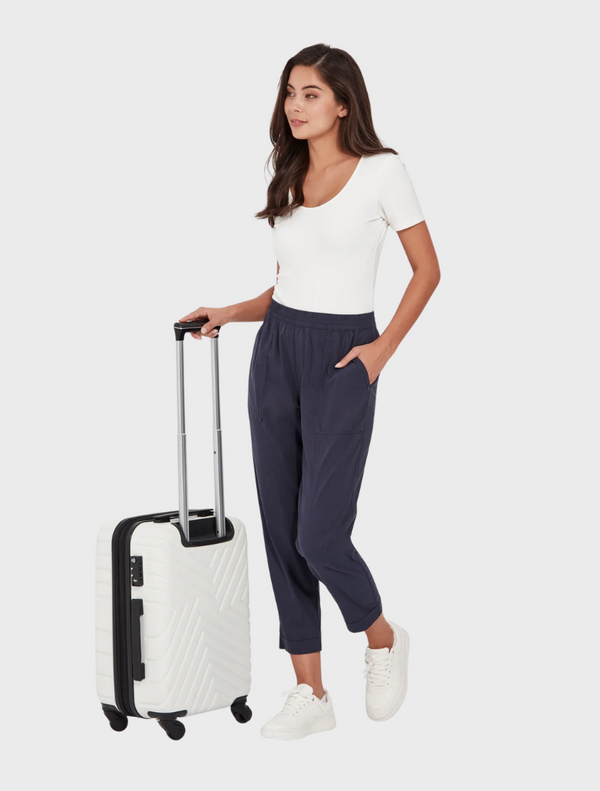 A woman in a white shirt and blue pants holds a suitcase, preparing for travel.