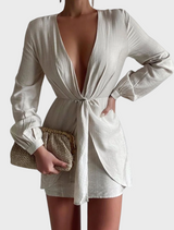 A woman in a flowing white dress poses with a natural Amalia pleated woven clutch featuring gold details.