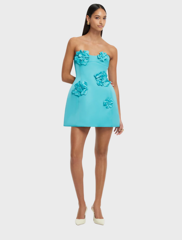 A model showcases a turquoise dress adorned with colorful flowers, highlighting a vibrant and stylish design.