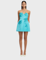 A model showcases a turquoise dress featuring a stylish ruffled skirt.