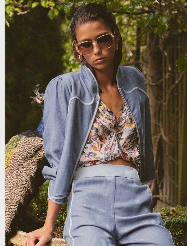 A woman in a blue jacket and pants sits on a bench, showcasing the Aurora Reversible Viscose & Tencel Fringe Jacket.