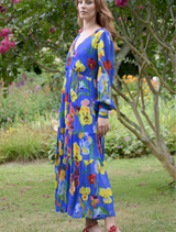 A woman in a cobalt floral dress stands gracefully, highlighting the dress's blue floral pattern.