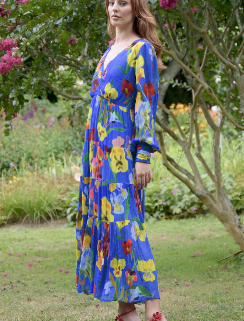 A woman in a cobalt floral dress stands gracefully, highlighting the dress's blue floral pattern.
