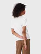 Back view of a woman in a cream round neck t-shirt and brown pants, standing casually.
