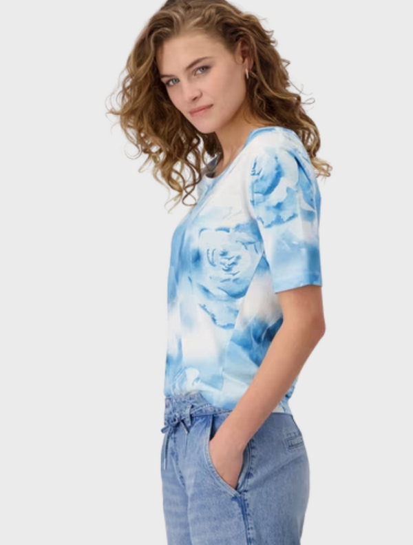 A model presents a blue and white tie-dye shirt, showcasing a dynamic and colorful swirl pattern.