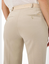 A woman showcases a casual outfit with beige trousers and a white shirt, embodying effortless style.