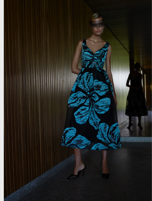 A woman wearing a blue dress and black shoes stands confidently, showcasing her stylish outfit.