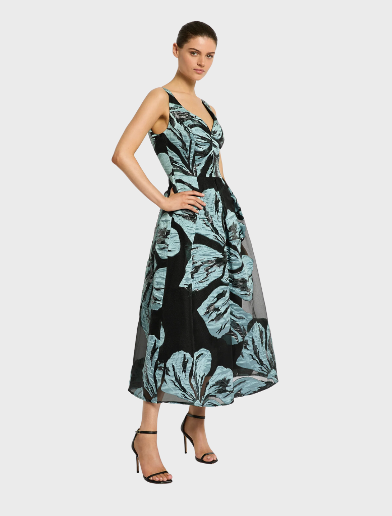  A woman dressed in a blue dress and black shoes stands, exuding a sense of style and grace.