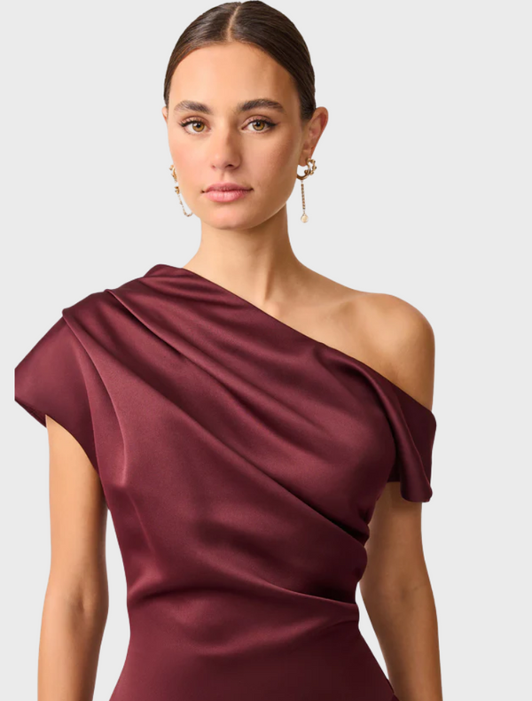 A satin burgundy dress with an asymmetric hem, showcasing a modern and chic design.
