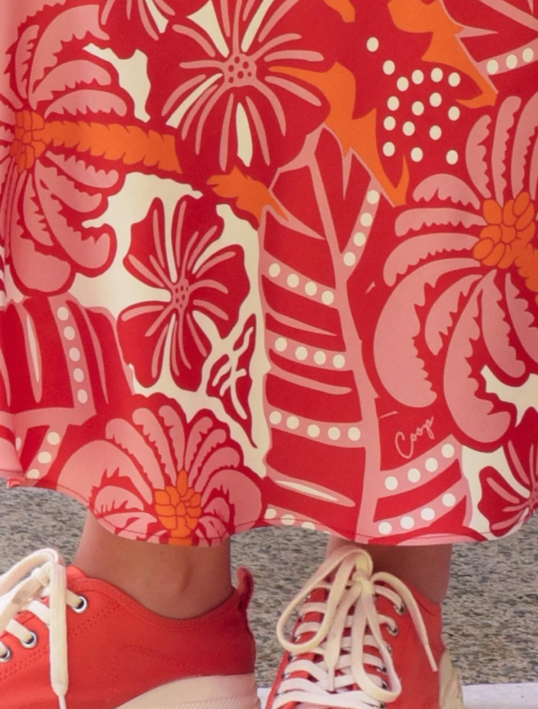 A woman showcases a pink sweater and red skirt, embodying a bright and fashionable look.