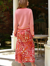 A woman in a pink sweater and red skirt smiles, displaying her stylish and cheerful attire.