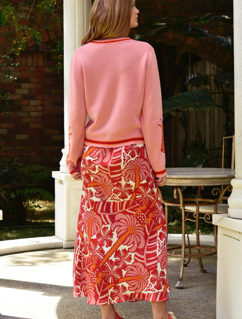 A woman in a pink sweater and red skirt smiles, displaying her stylish and cheerful attire.