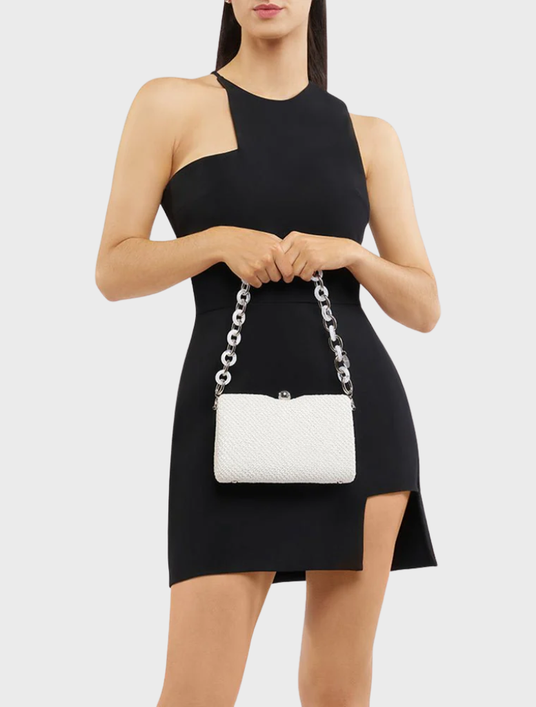 A woman in a black dress holds a white Birdie Textural Handle Bag, showcasing a stylish contrast in her outfit.