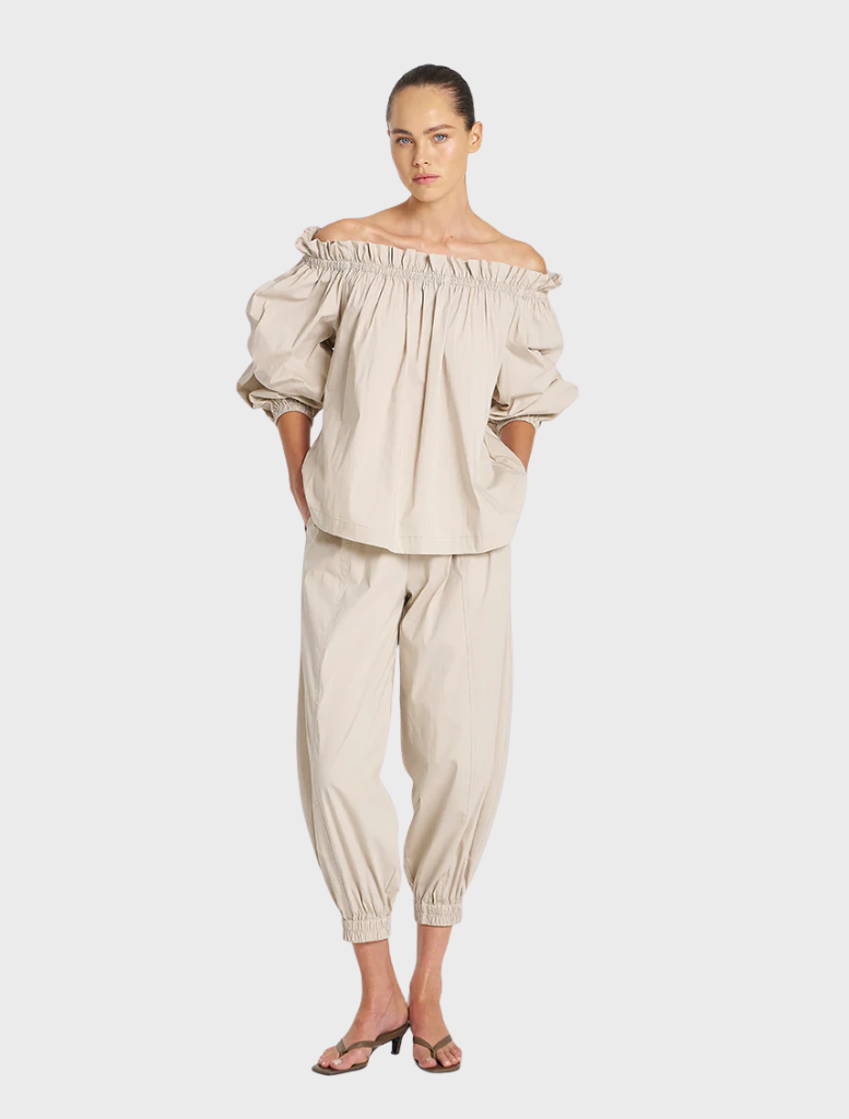 A model wears an elegant off-the-shoulder top with fitted pants, presenting a trendy and sophisticated look.
