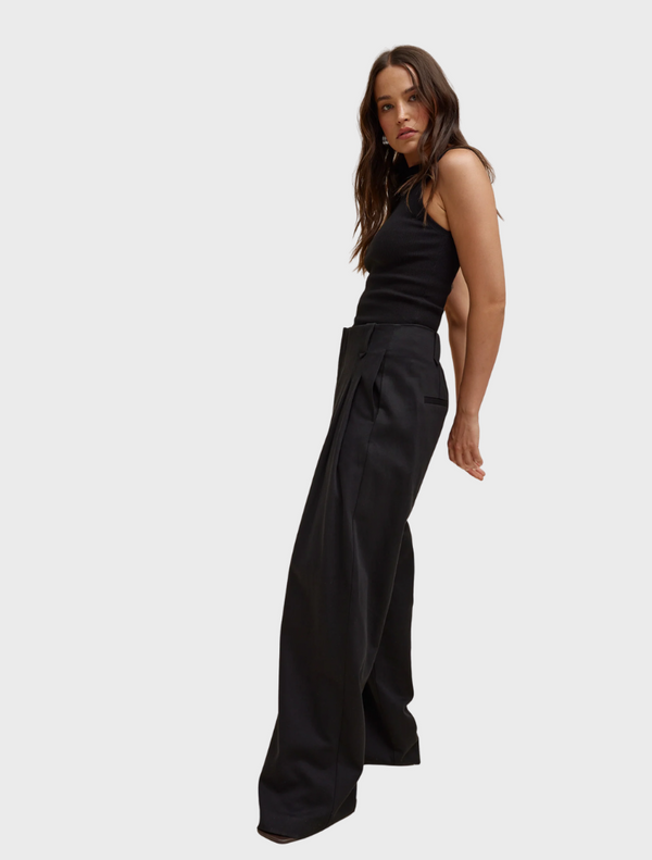 A model poses in stylish black pants paired with a matching top, showcasing a sleek and modern outfit.