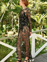 A woman in a black lace dress and sandals poses gracefully, highlighting her fashionable ensemble.