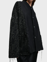 Black unisex oversized jacket made of wool-blend brocade and soft wool flannel, featuring two front pockets and decorative cords.