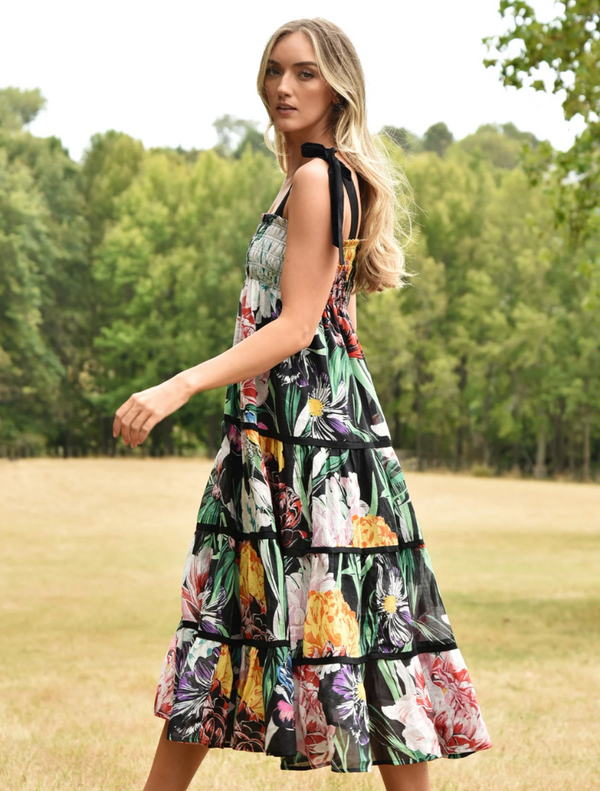 A woman is dressed in a floral print dress, featuring a lively pattern of flowers in bright colors.