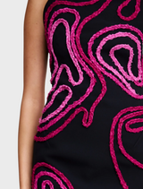 A stylish black dress adorned with a pink swirl design, highlighting a unique and fashionable look.