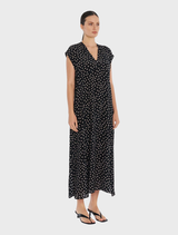 The image shows a woman wearing a black polka dot maxi dress, known as the Maxi Slice Dress - Black/Meringue.