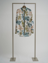 A lime multi tropical print blouse is displayed hanging on a stand.
