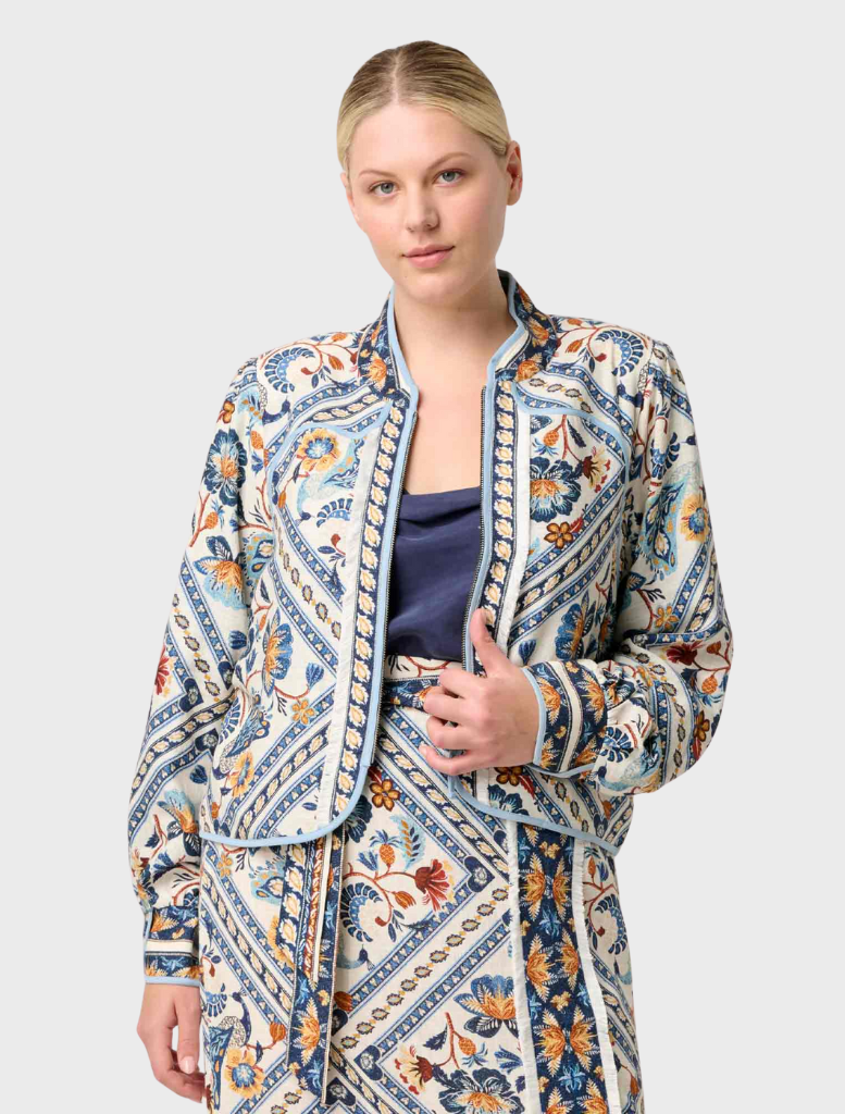 A woman in a blue jacket and pants is perched on a bench, wearing the Aurora Reversible Viscose & Tencel Fringe Jacket.