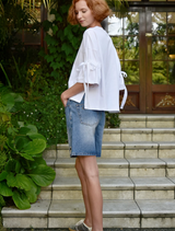 A woman in a white shirt and denim shorts smiles while standing in a vibrant outdoor environment.