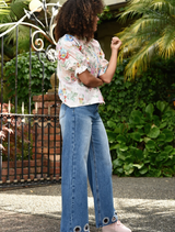 A woman in a floral shirt and jeans poses confidently for the camera.