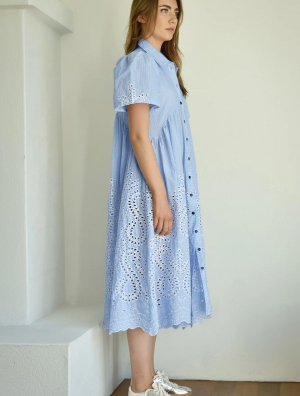 A woman in a blue dress featuring elegant white lace accents poses confidently.