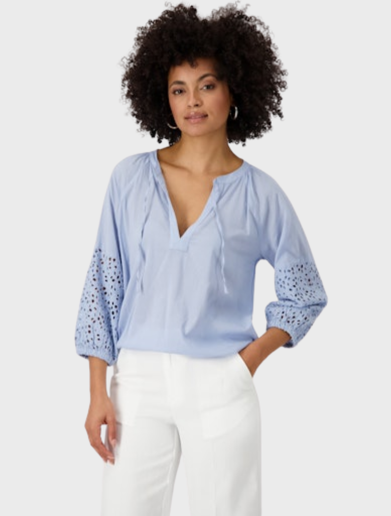 Blue lace-sleeved blouse paired with white pants, showcasing an elegant openwork pattern.