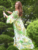 A woman dressed in a floral pattern walks along a path in a park, with lush greenery surrounding her.