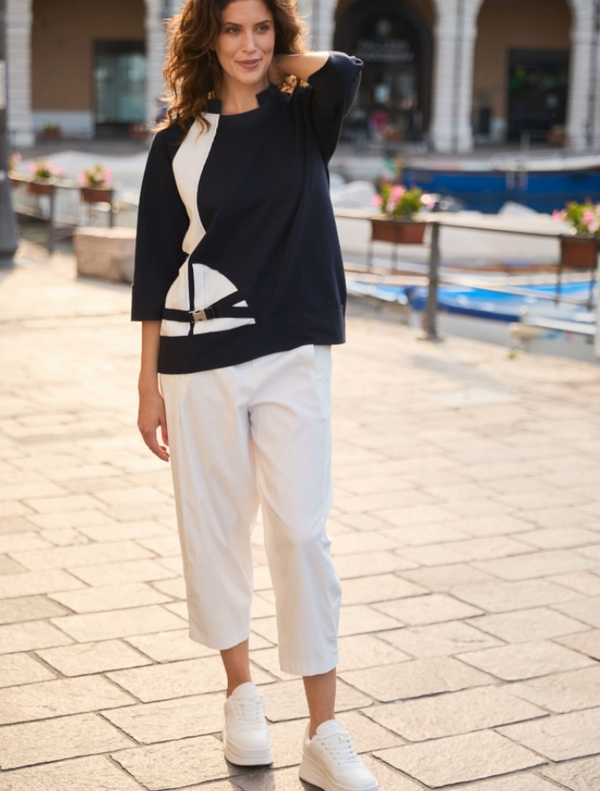 A woman wearing a navy and white color block top and white pants stands confidently on a dock.
