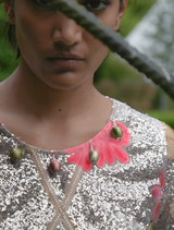 A woman in a silver and pink floral dress leans against a tree, embodying elegance in a serene outdoor scene.